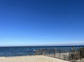 A beach with a clear blue sky, calm sea, and a wooden fence.
