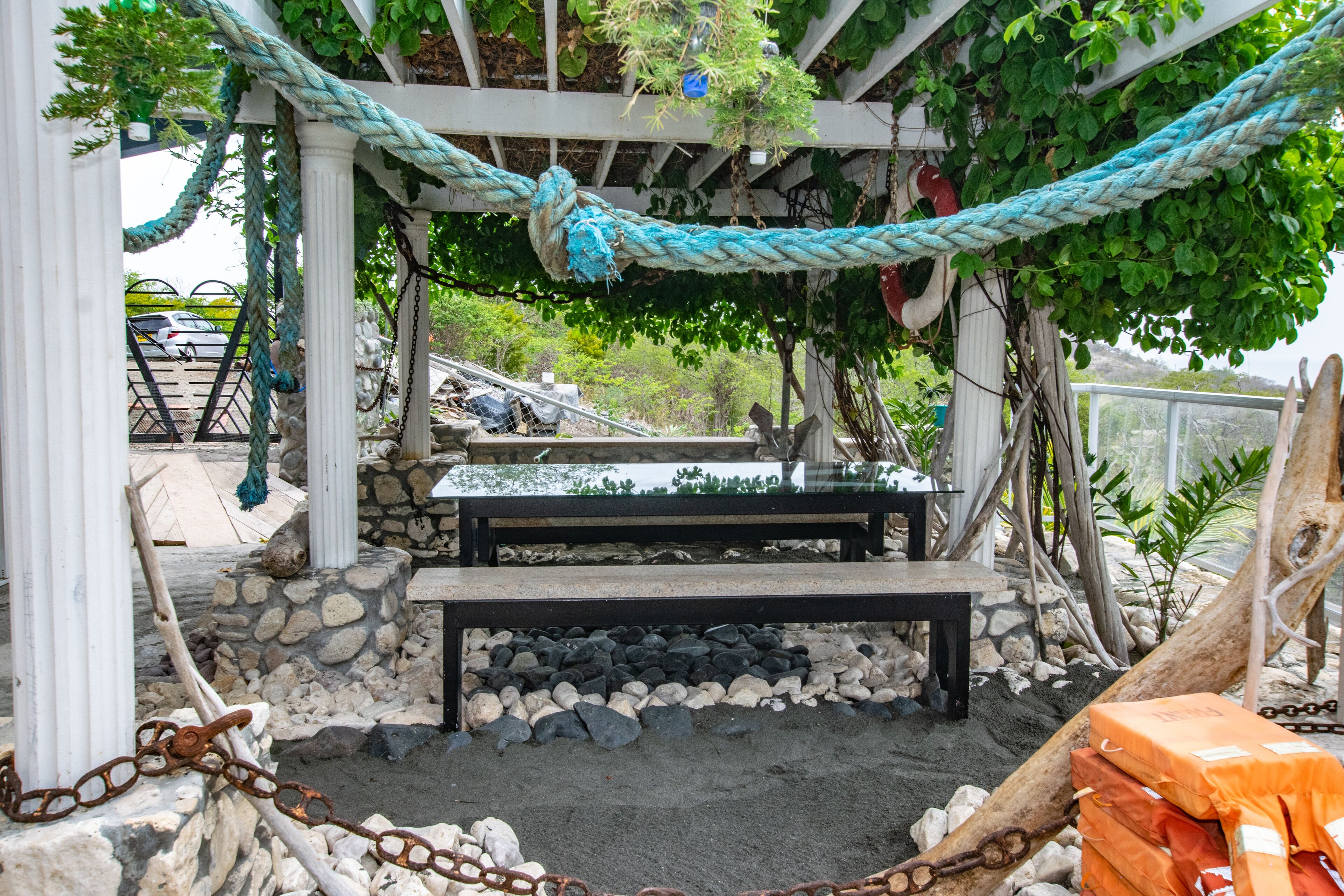 A covered outdoor seating area with a stone wall, a wooden bench, and a rope swing.