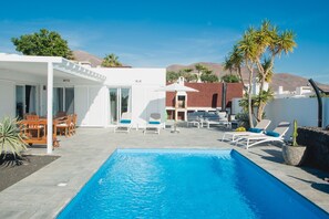 A modern outdoor pool area with a clear blue pool, lounge chairs, and a dining set. - Exclusive luxury villa with private pool, Las Coloradas, Playa Blanca, Lanzarote, ocean view (Playa Blanca)