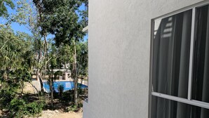 En vy över en swimmingpool omgiven av träd och en byggnad med en vit fasad och ett fönster med gardiner.
