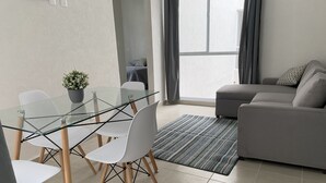 Ett modernt vardagsrum med ett matbord i glas, vita stolar, en grå soffa och en mönstrad matta.