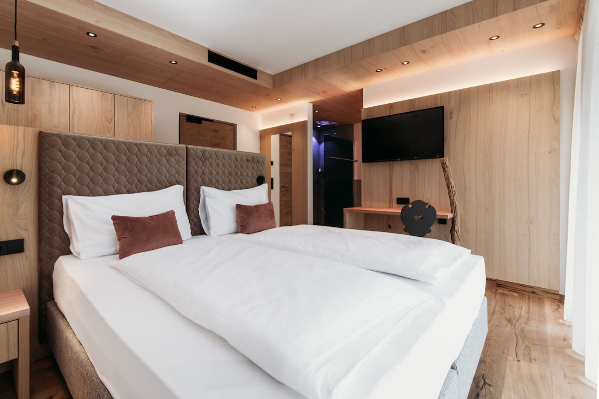 Une chambre moderne avec un grand lit, des murs recouverts de panneaux en bois, un téléviseur fixé au mur et un banc intégré.