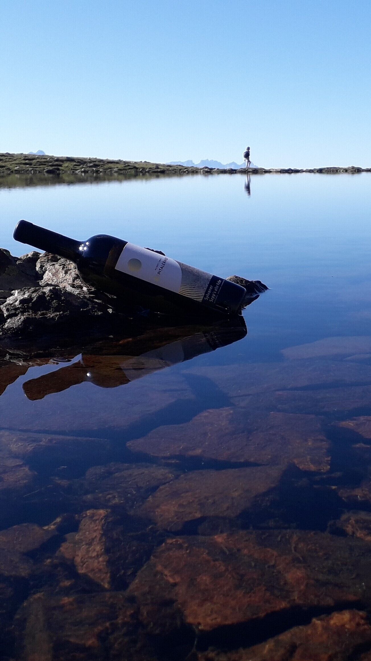 A telescope on a rock by a calm lake with a person in the distance.