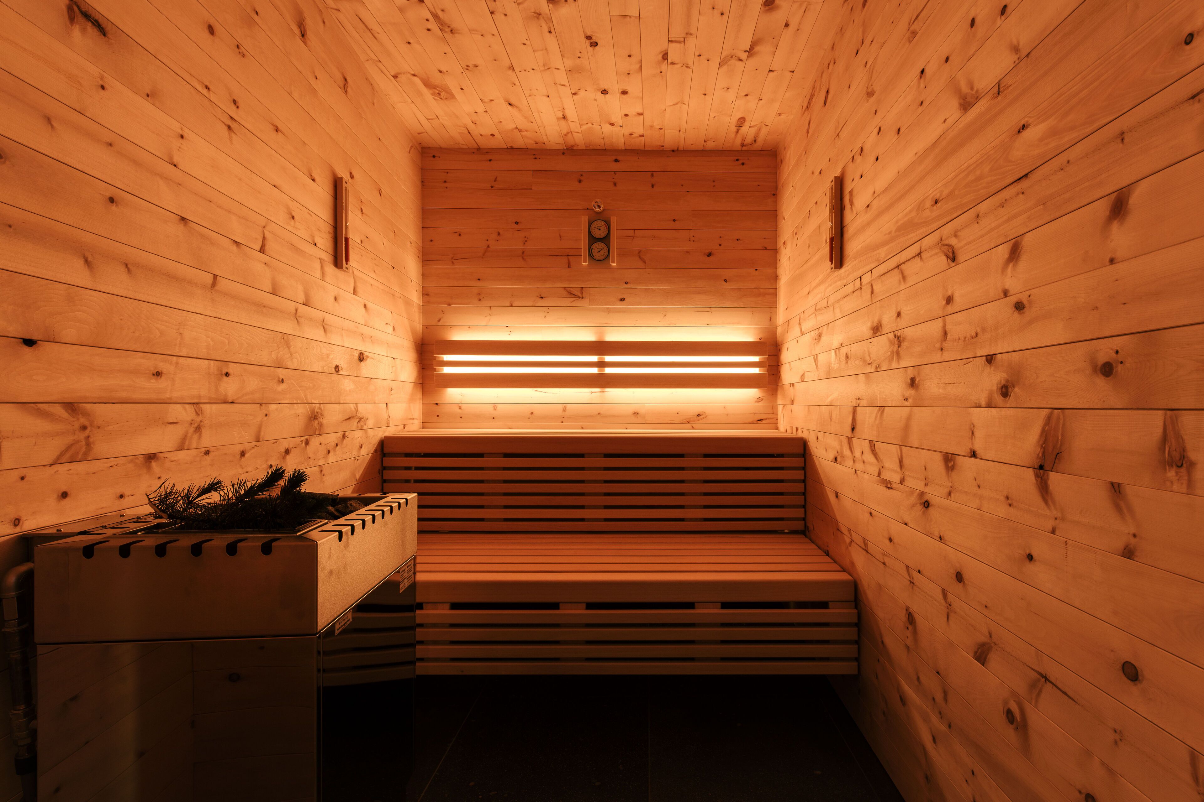 A sauna with wooden walls and benches, featuring a central light fixture and a small window.