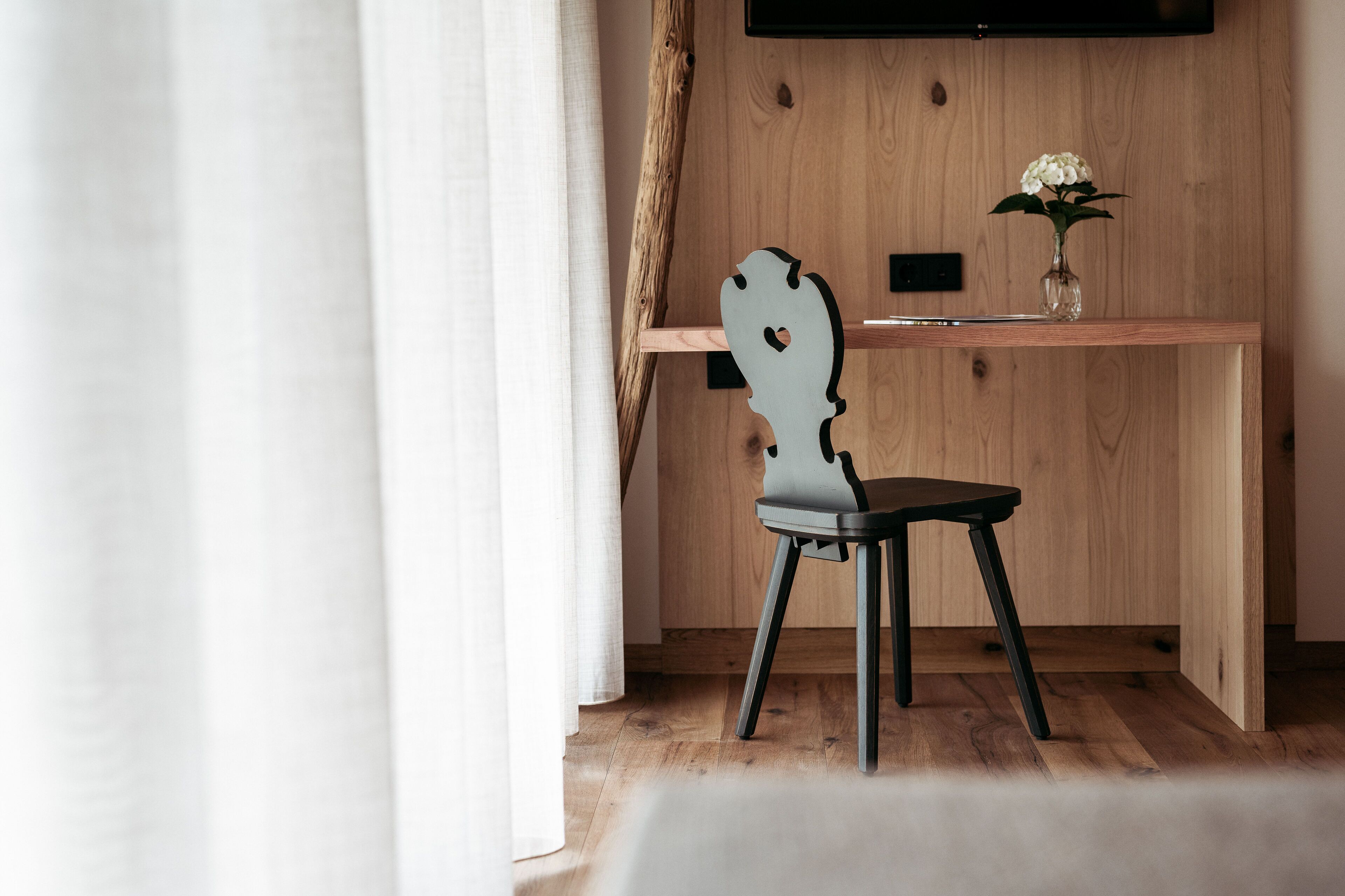 Un bureau en bois orné d’un vase de fleurs, une chaise dotée d’un dossier au design original et un mur en bois.