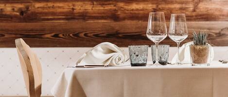 A wooden wall with framed photos, a table set with wine glasses and a potted plant.