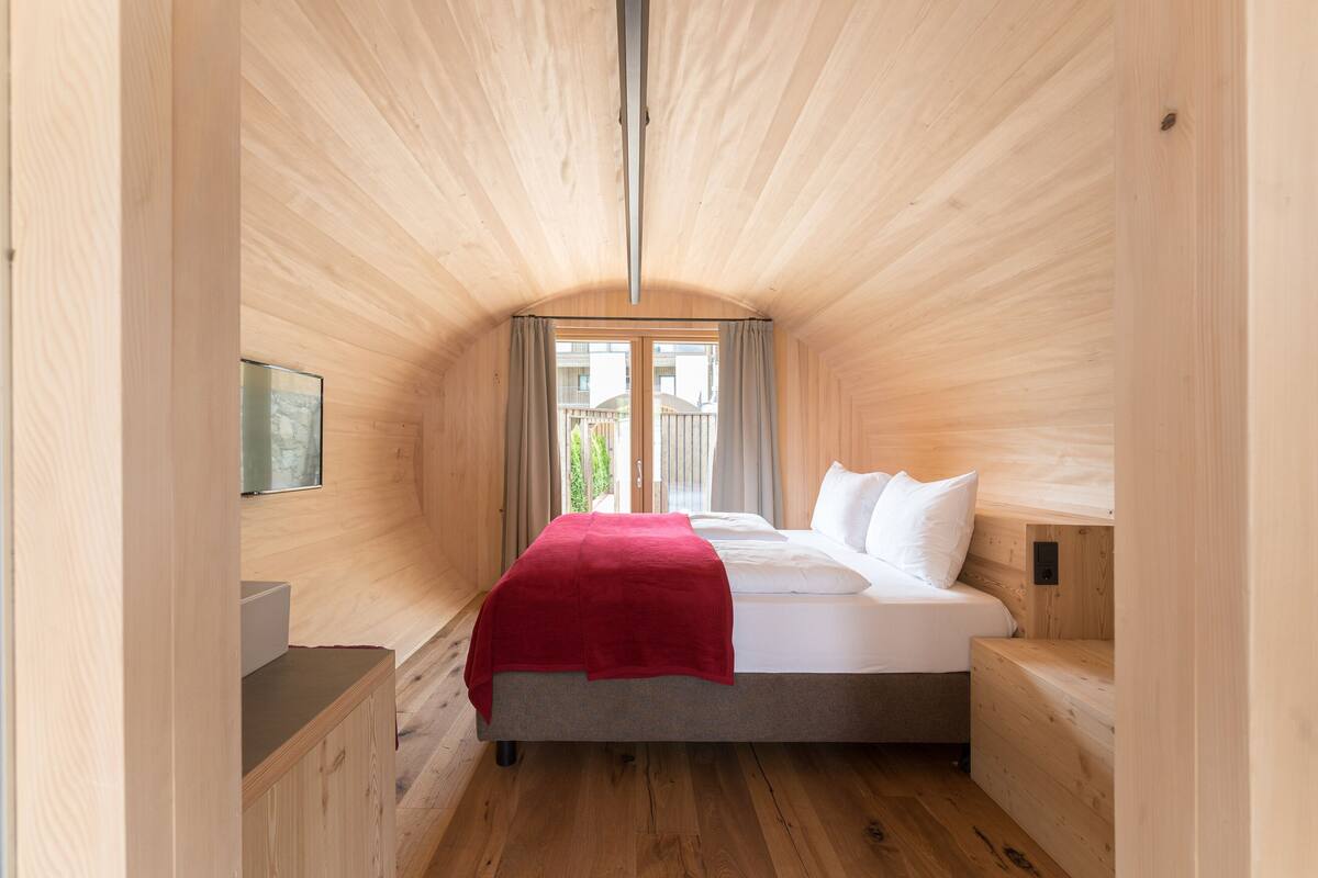 Une petite pièce en bois, avec un lit, une petite table de chevet et une fenêtre avec des rideaux.