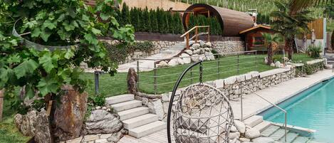 A pool area with a hanging chair, stone steps, and a wooden deck.