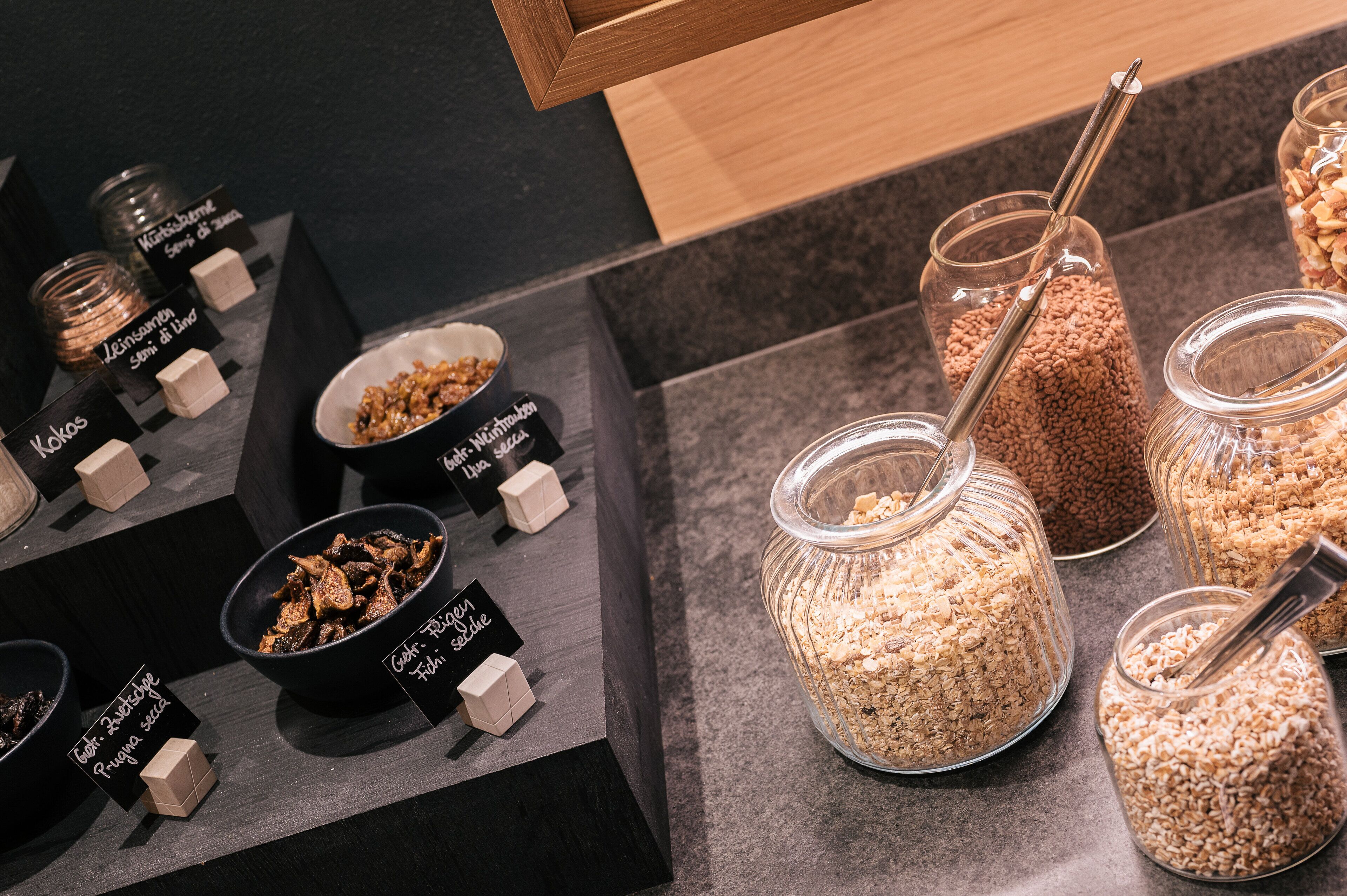 A display of various food items in glass jars and bowls with labels, arranged on a countertop.