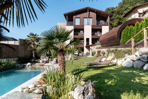 A modern building with a pool, surrounded by a well-maintained lawn and rocks. - Weingut und Genusshotel Spitalerhof (Chiusa)