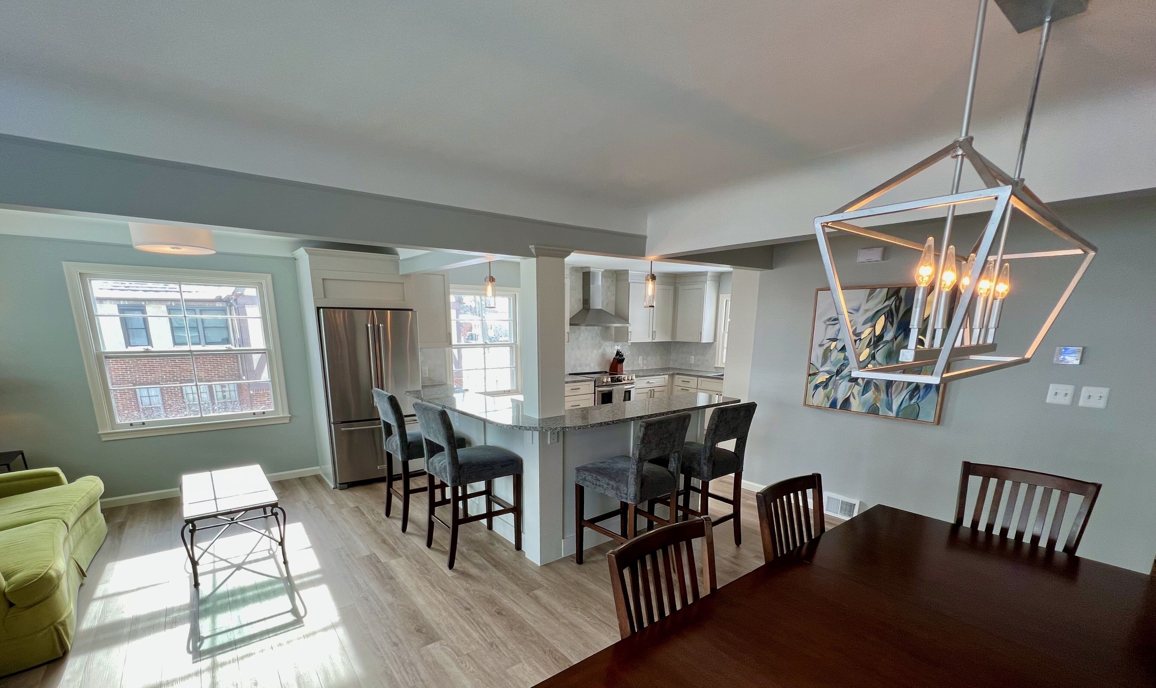A modern kitchen with a central island, dining area with chairs, and a large window.