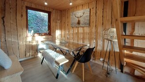 A wooden cabin interior with a dining table, bench, and a wall-mounted lamp.