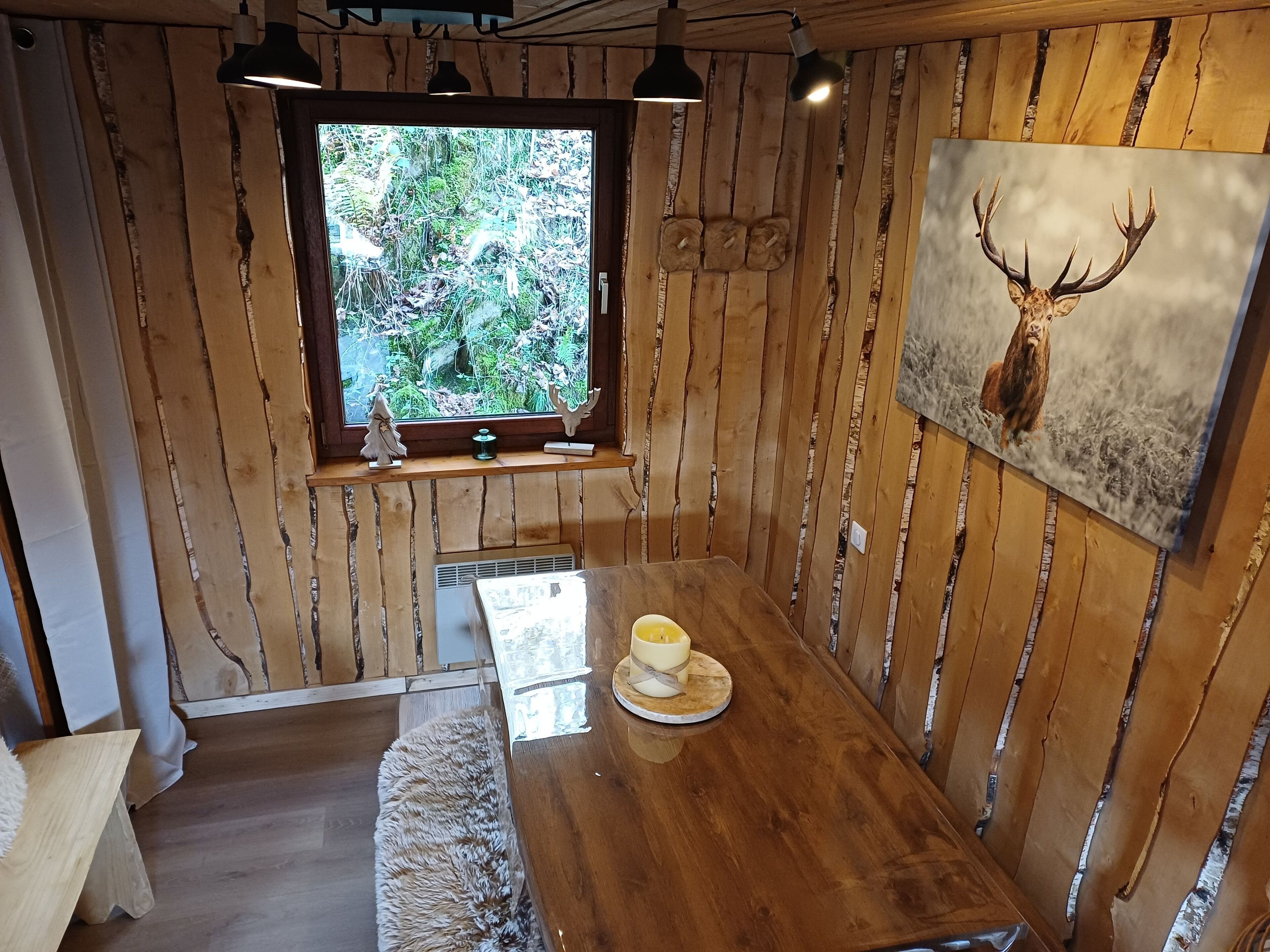 Ein Holzinnenraum mit Fenster, einem Hirschkopf-Gemälde und einem Tisch mit einer Tasse.
