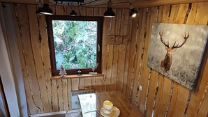 A wooden interior with a window, a painting of a deer head, and a table with a cup.