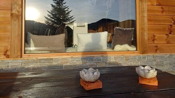 A wooden cabin with a large window reflecting a snowy landscape, a stone fireplace, and two decorative lotus-shaped vases on the mantel.