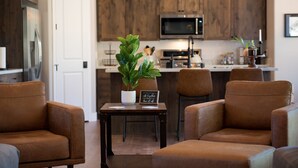 A modern kitchen with wooden cabinets, a microwave, and a dining area with brown leather chairs and a small table with a plant and a sign. - Custom 4bd Mountain & Golf Retreat, Sleeps 8,
A/C, Close to All Key Attractions (Williams)