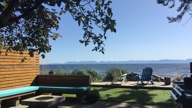 A patio with a wooden bench, a grill, and a view of the water and mountains.