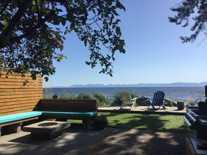 A patio with a wooden bench, a grill, and a view of the water and mountains. - Perfectly Chic Waterfront Cottage Top Floor (Roberts Creek)