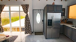 Een moderne keuken met een roestvrijstalen koelkast, een groot raam met patroon gordijnen en uitzicht op de omgeving.
