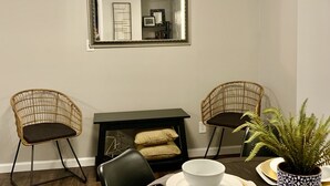 A dining area with a round table set for four, two wicker chairs, a black console table with a mirror, and a potted fern.