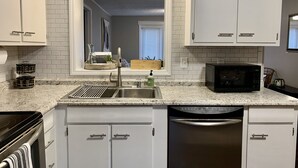 A kitchen with white cabinets, a stainless steel sink, a microwave, and a dishwasher.