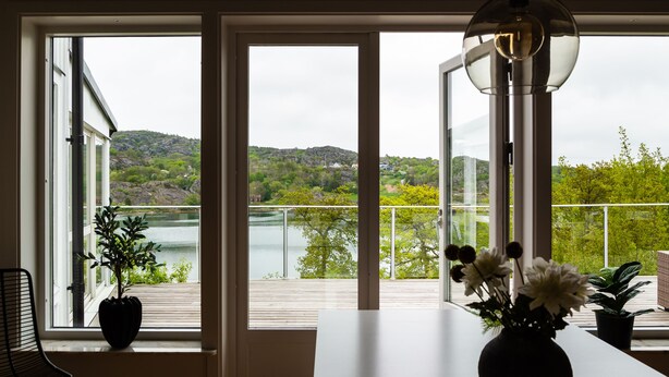 A room with large windows overlooking a lake and hills, a table with a vase of flowers, and a chair. - Exclusive house with private boathouse (Västra Götalands län)