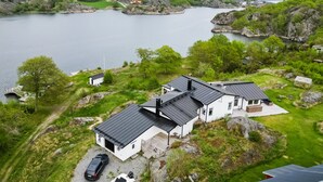 A lakeside property with a white building, a boat, and a car parked by the water. - Exclusive house with private boathouse (Västra Götalands län)