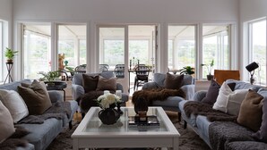 A spacious living room with large windows, two sofas, a coffee table, and a dining area visible through the glass doors. - Exclusive house with private boathouse (Västra Götalands län)