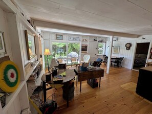 A spacious living room with a wooden floor, a dining table, and a kitchen area visible through an open door.