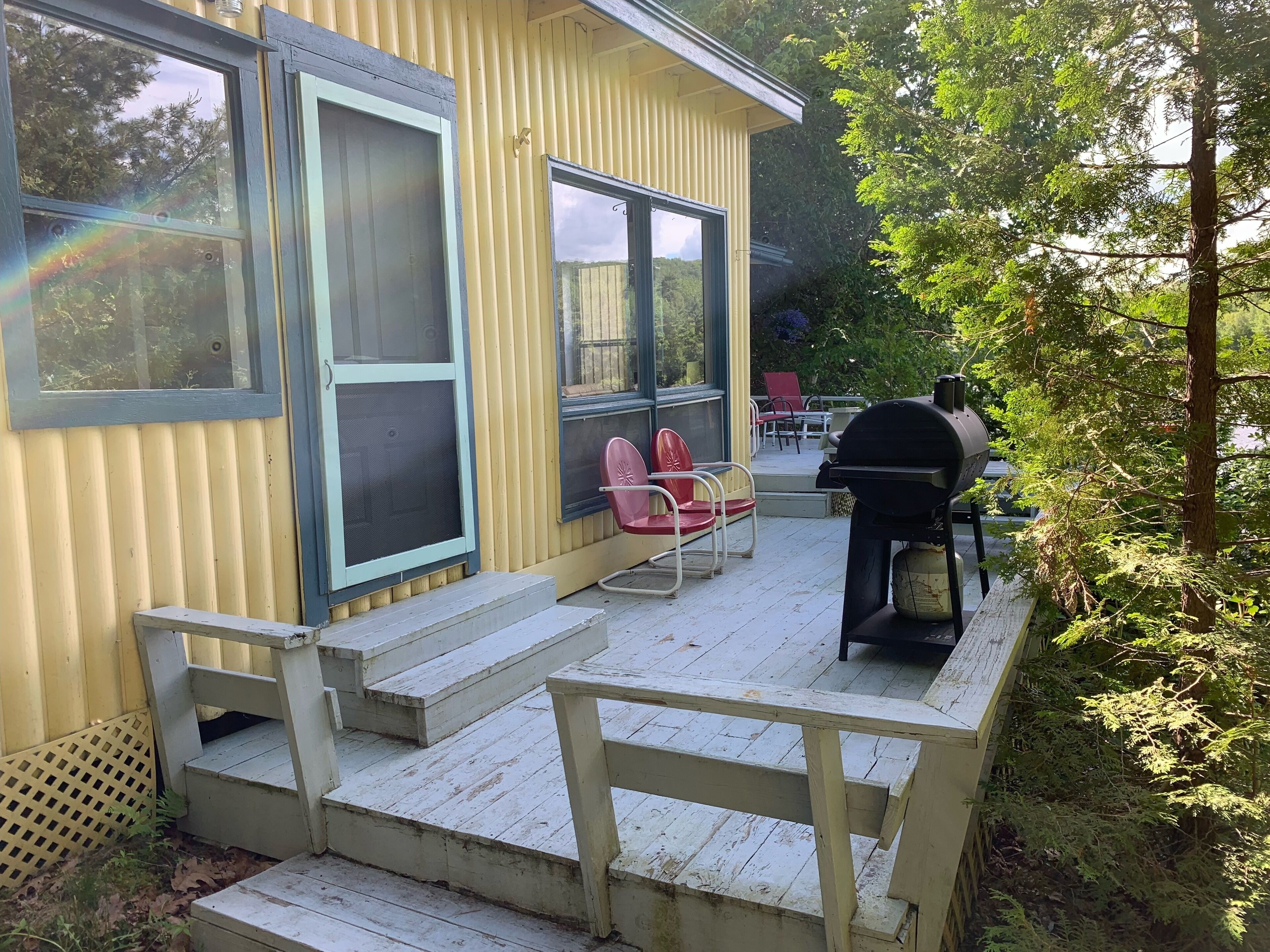 Un bâtiment jaune doté d’un porche abrité, d’un espace extérieur aménagé pour s’asseoir et d’un barbecue.