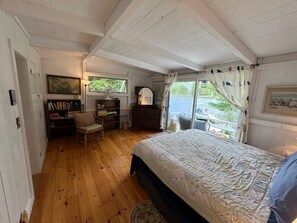 Une chambre avec un plancher en bois, un lit, un bureau, une chaise et une fenêtre avec des rideaux.