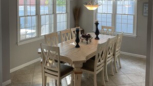 Uma sala de jantar com mesa de madeira, cadeiras brancas e um lustre.
