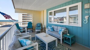 Ein Balkon mit Blick auf den Strand, ein weißes Sofa, türkisfarbene Stühle und ein kleiner Tisch.