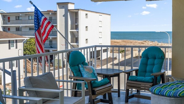 Een balkon met twee turquoise stoelen en een kleine tafel, met uitzicht op een strand en zee.