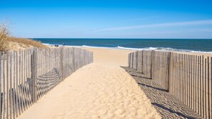 Ein Sandweg am Strand, der zum Meer führt, gesäumt von Holzzaun.
