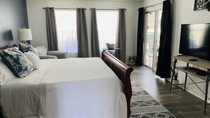 A hotel room with a large bed, a desk with a TV, and a view of the outdoors through the windows. - Quiet Family Friendly Saltwater Pool Home, Near Beach (Navarre)