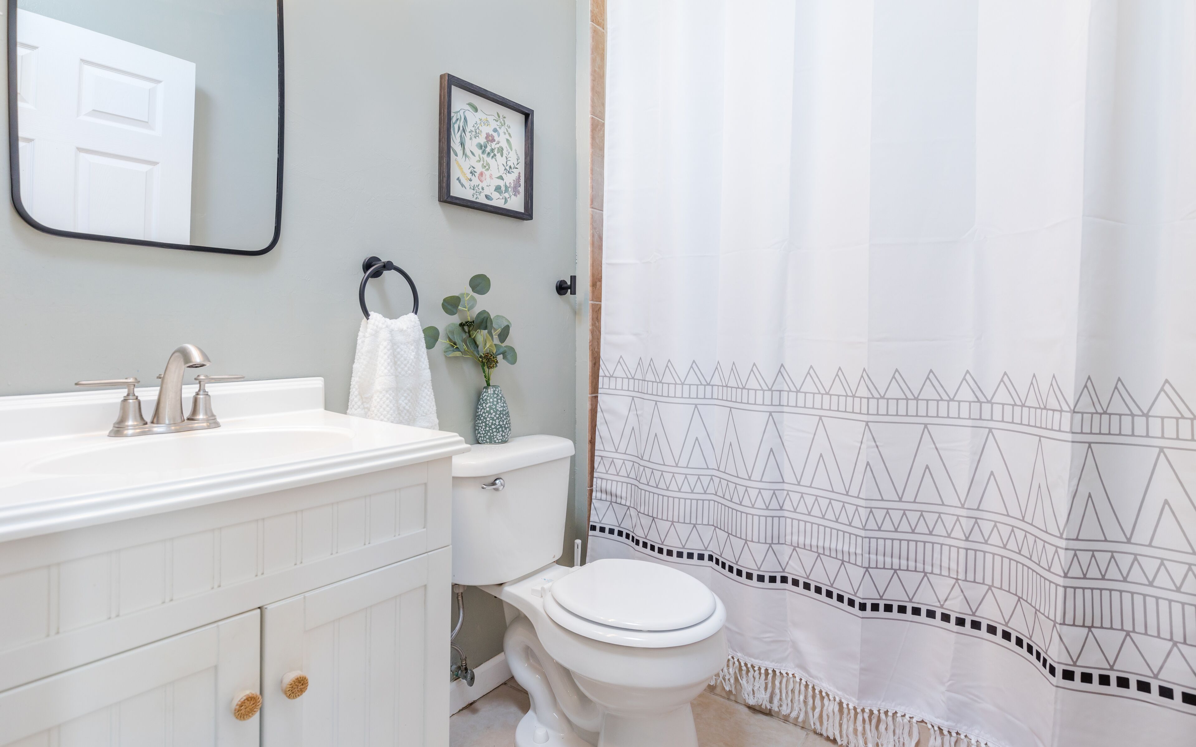 Een badkamer met een witte wastafel, toilet en een douchegordijn met een geometrisch patroon.