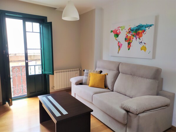 A living room with a beige sofa, a coffee table, a world map artwork, and a window with a view. - Apartment in the Old Town of Ourense **** Solaina das Burgas **** (Ourense)