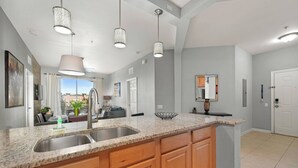 A kitchen with granite countertops, wooden cabinets, a double sink, pendant lights, and a view of the city through large windows.