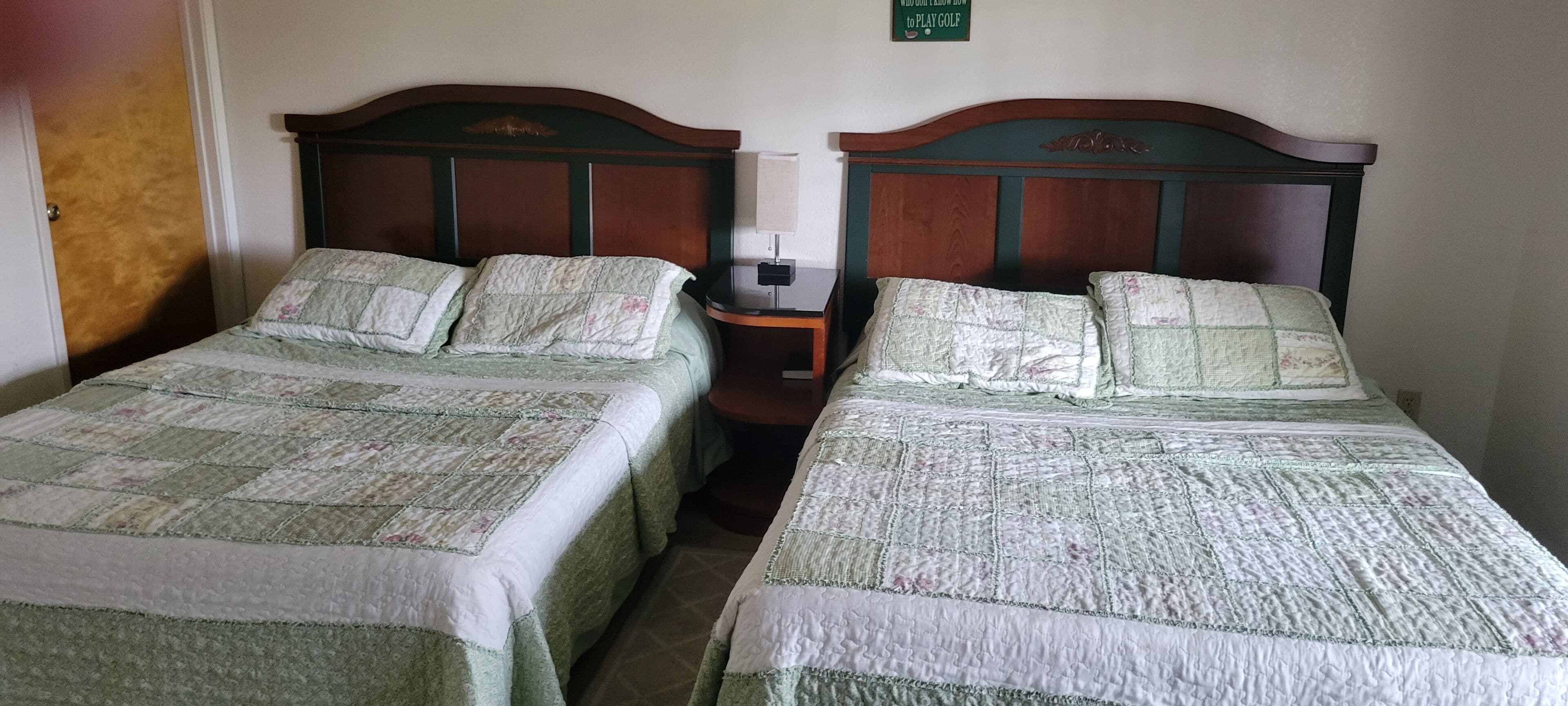 Dos camas individuales con cabeceras y pies de cama iguales, una mesita de noche con lámpara, y un cartel sobre las camas.