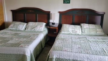 Dos camas individuales con cabeceras y pies de cama iguales, una mesita de noche con lámpara, y un cartel sobre las camas.