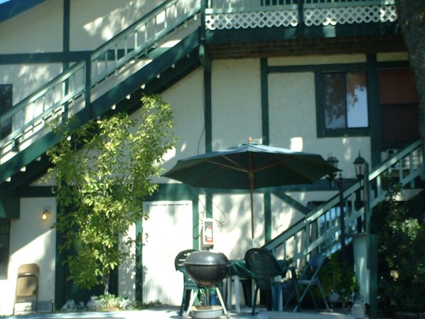 A covered outdoor seating area with a grill, chairs, and an umbrella. - The 10th Green Inn (Valley Springs)