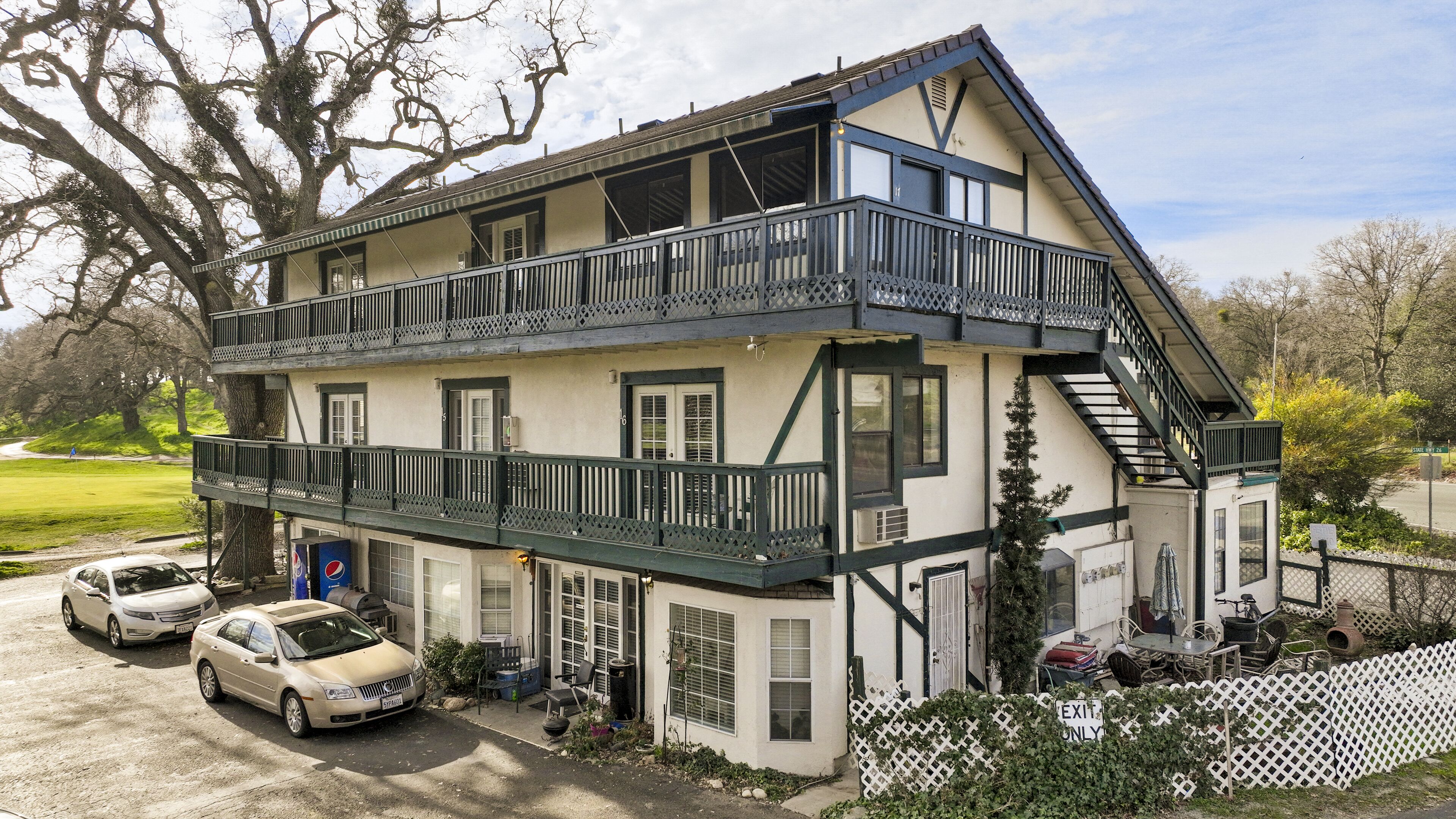 A two-story building with a balcony, a garage, and a driveway with parked cars.