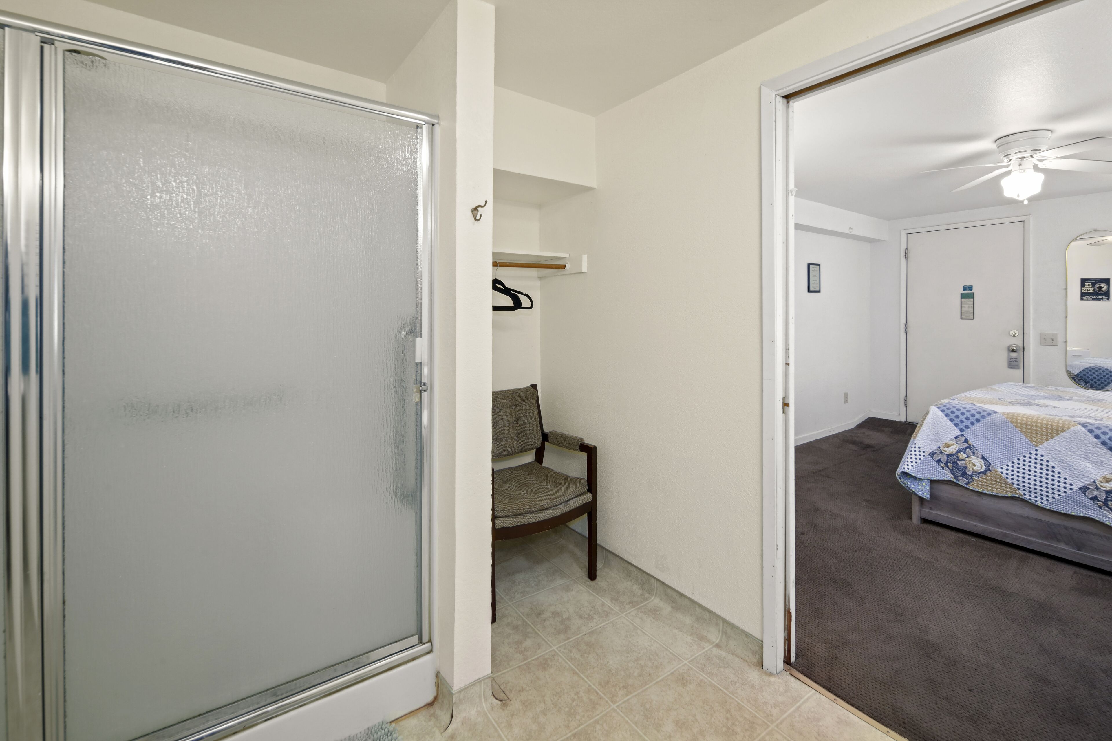 A bedroom with a bed, a chair, and a door leading to another room.