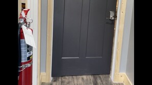 A closed dark grey door with a keypad lock, a wooden frame, and a doormat on a wooden floor. - Romantic king suite located 15 minutes from U of I (Saint Joseph)
