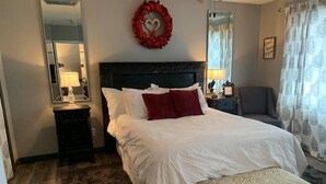 A neatly arranged bedroom with a large bed, a bedside table with a lamp, a chair, and a mirror on the wall. - Romantic king suite located 15 minutes from U of I (Saint Joseph)