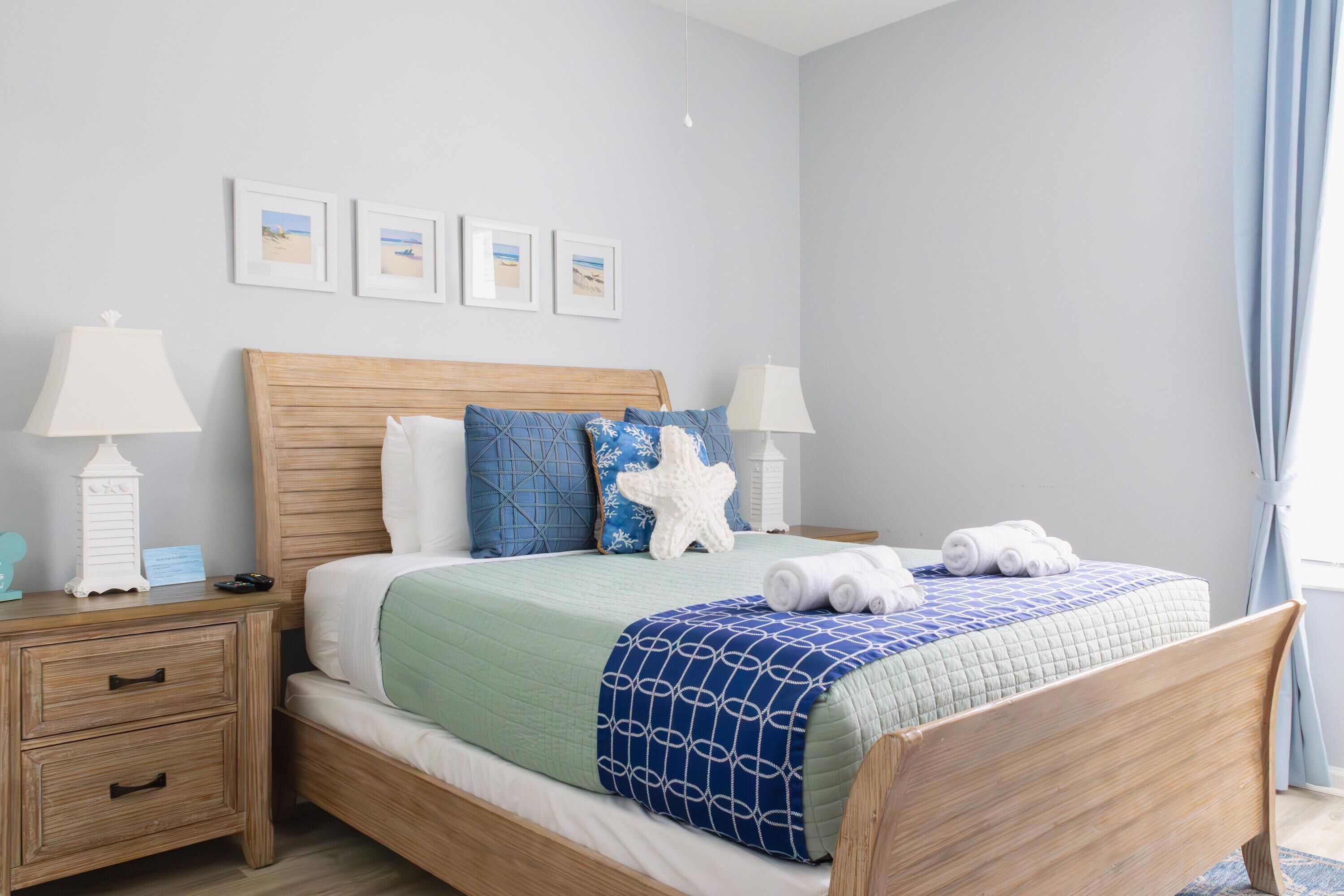 A neatly arranged bedroom with a wooden bed, two bedside tables, a nightstand, and a wall with framed pictures.