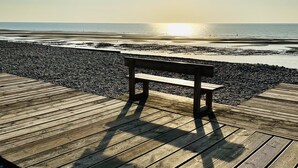 En träbrygga med en bänk, med utsikt över en stenstrand och havet.