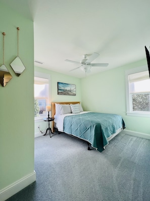 A bedroom with a bed, a nightstand, a ceiling fan, and a window.
