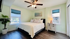 Une chambre à coucher avec un lit, un ventilateur de plafond, une table de chevet, une lampe et une fenêtre donnant sur un beau paysage.